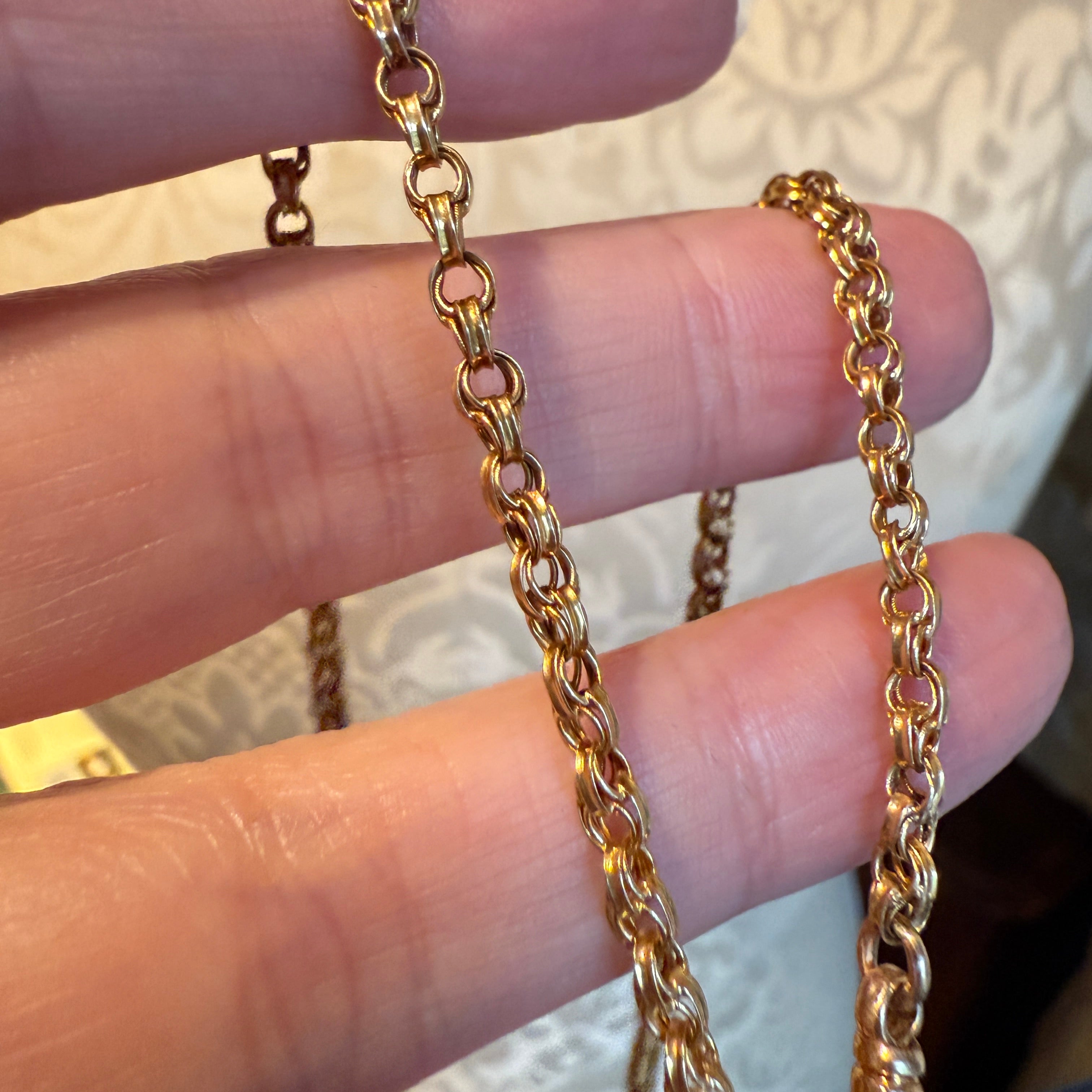 antique Gold watch chain held between fingers with a blurred background